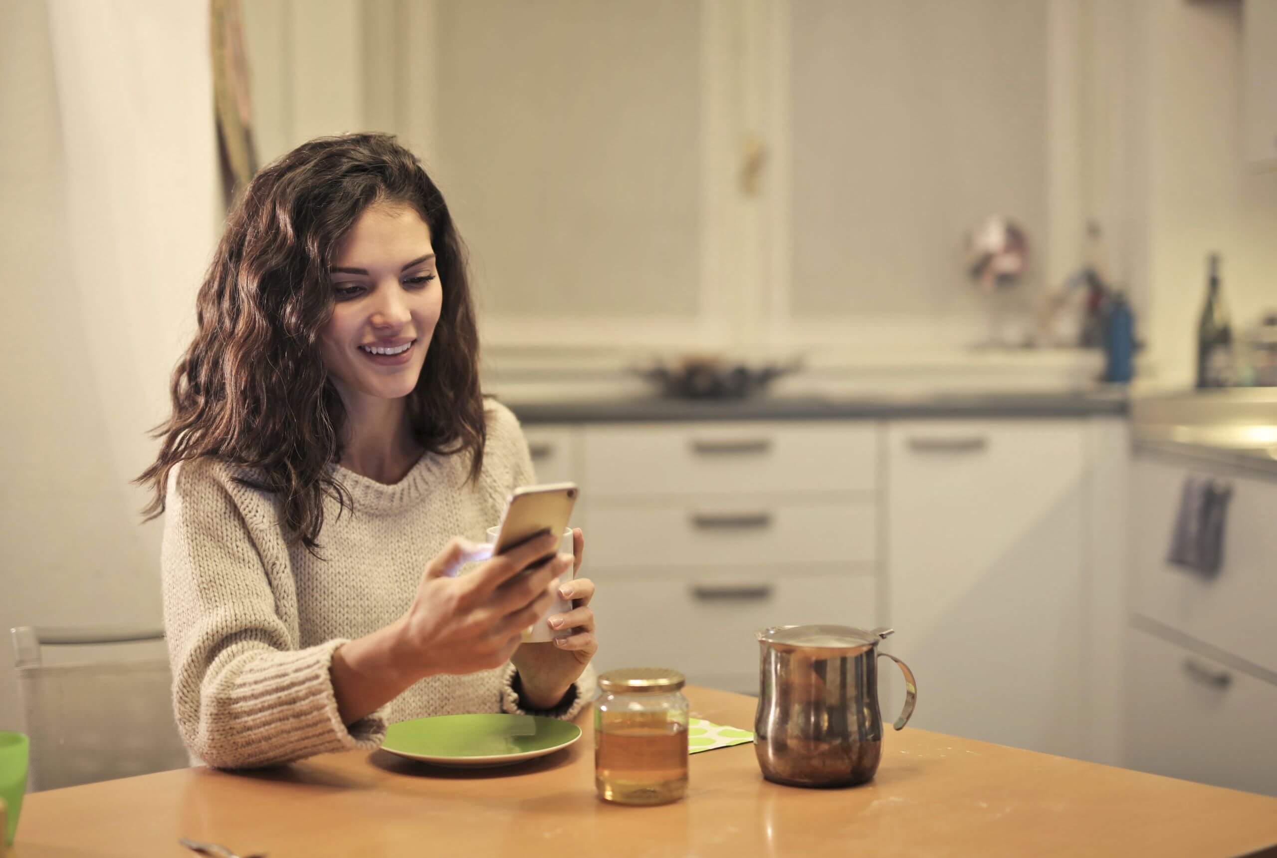 Young woman sitting at kitchen table with her phone and a cup of tea