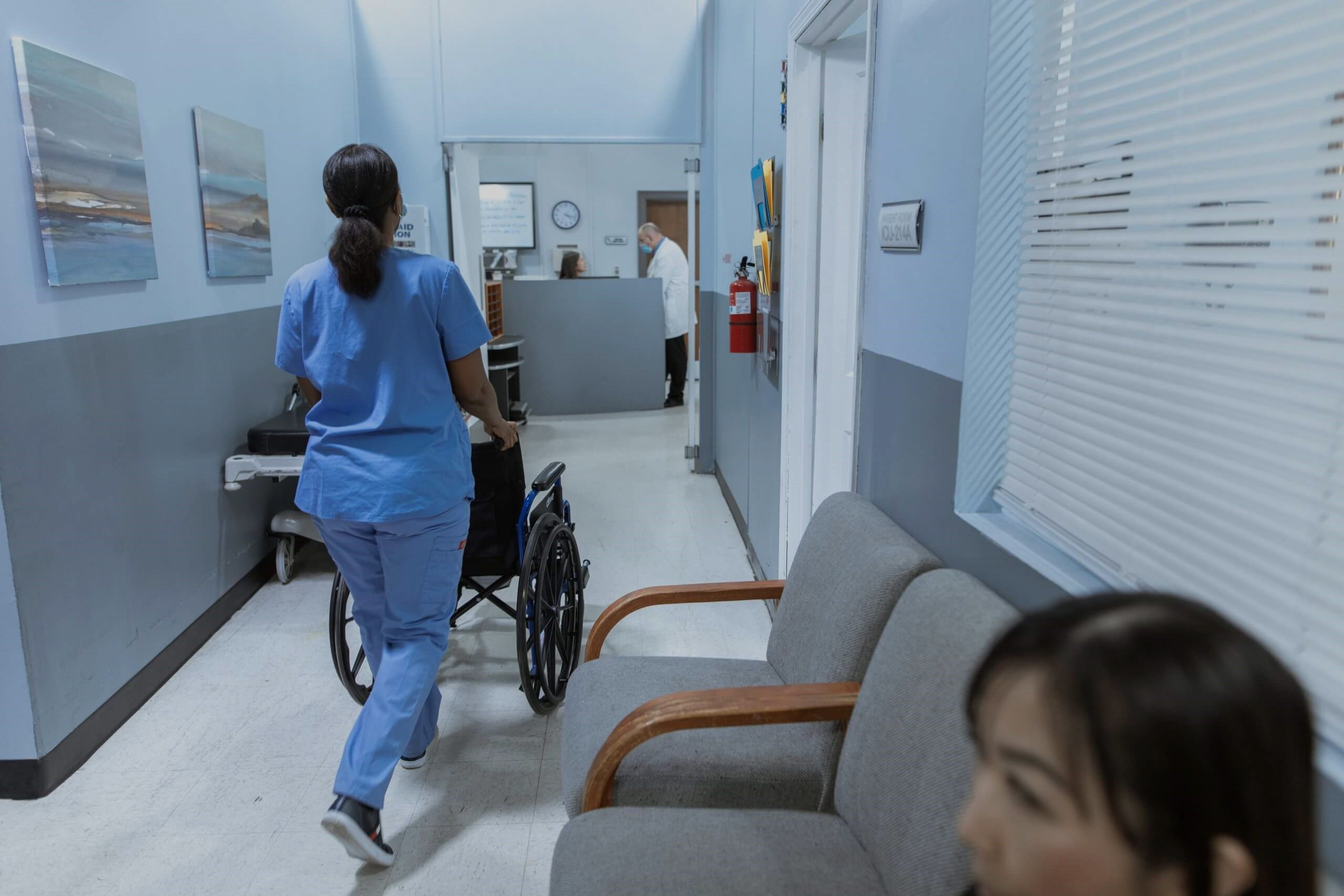 Nurse pushing a wheelchair down a clinic corridor