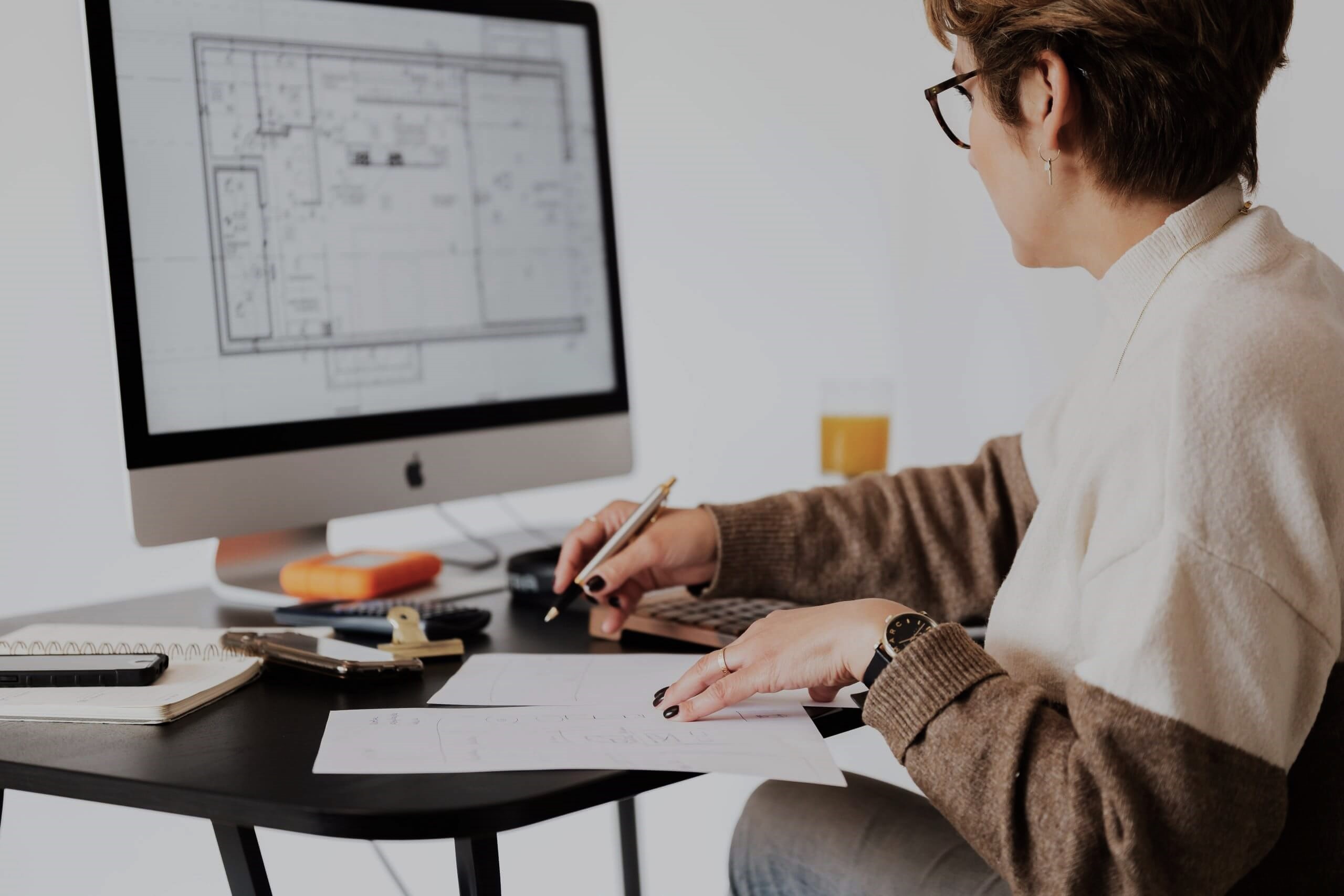 Woman sitting in front of computer, looking at blueprints