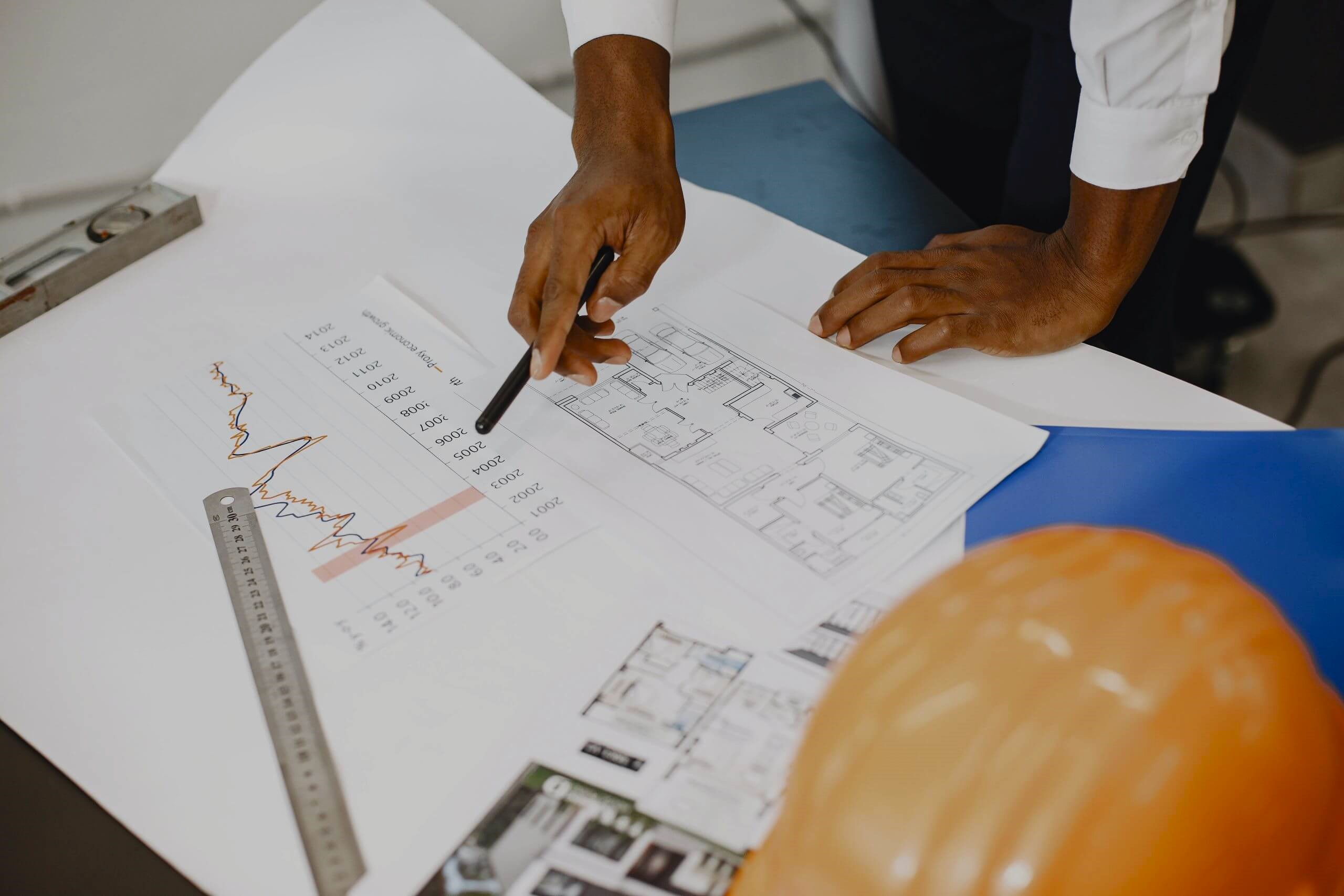 Hands pointing at floorplan on a table with a hard hat next to it